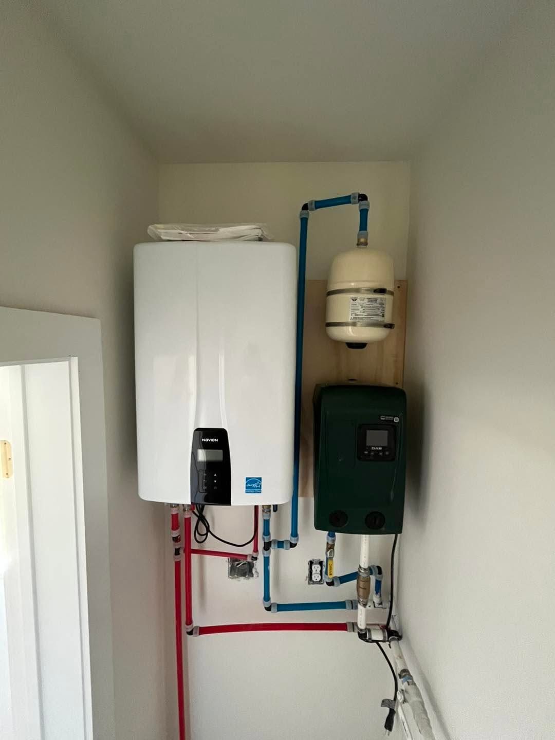 Wall-mounted boiler and water heater with visible blue and red piping in a small utility room