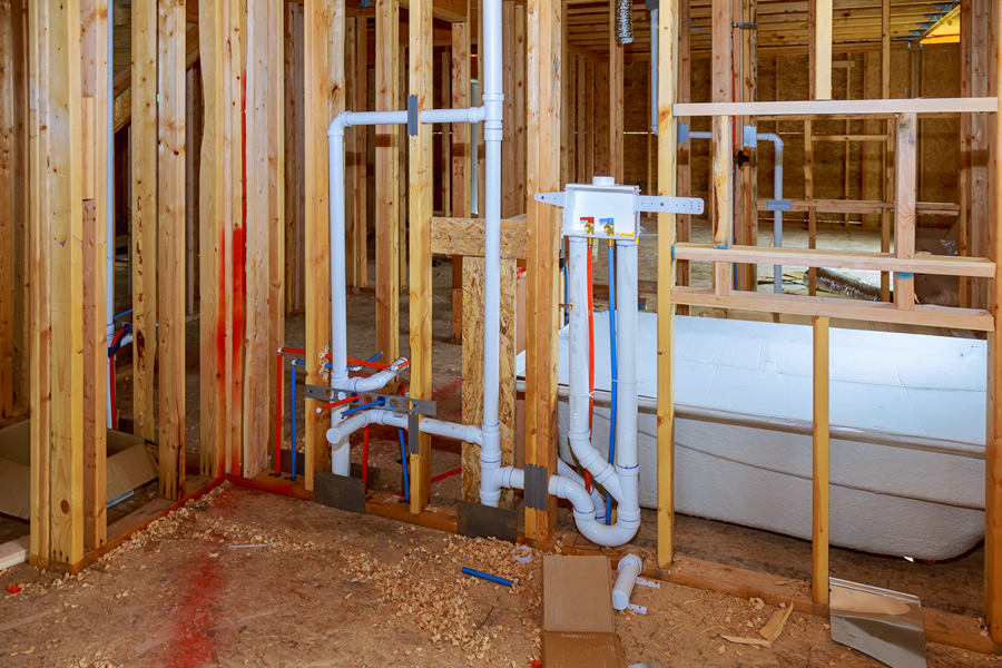 Exposed plumbing pipes and fixtures inside an unfinished room with wooden framing and a bathtub.