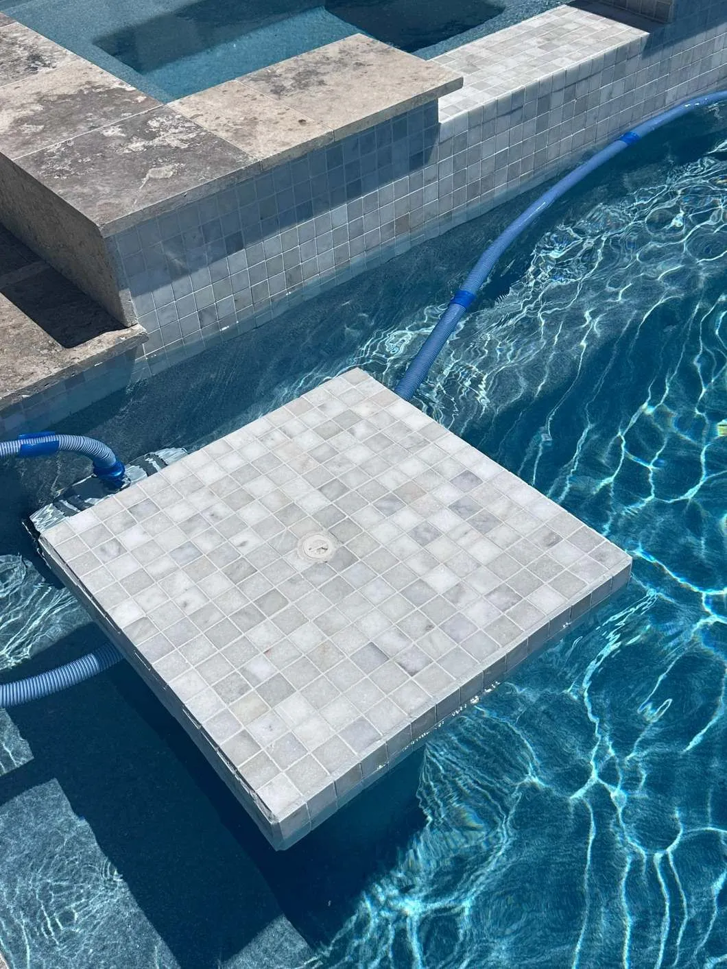 A tile sitting on the edge of a swimming pool next to a hose.