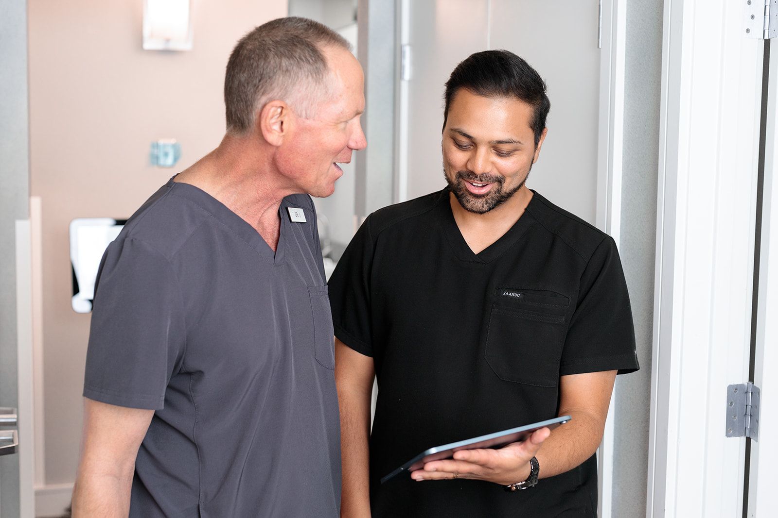 Two men in scrubs are standing next to each other and looking at a tablet.