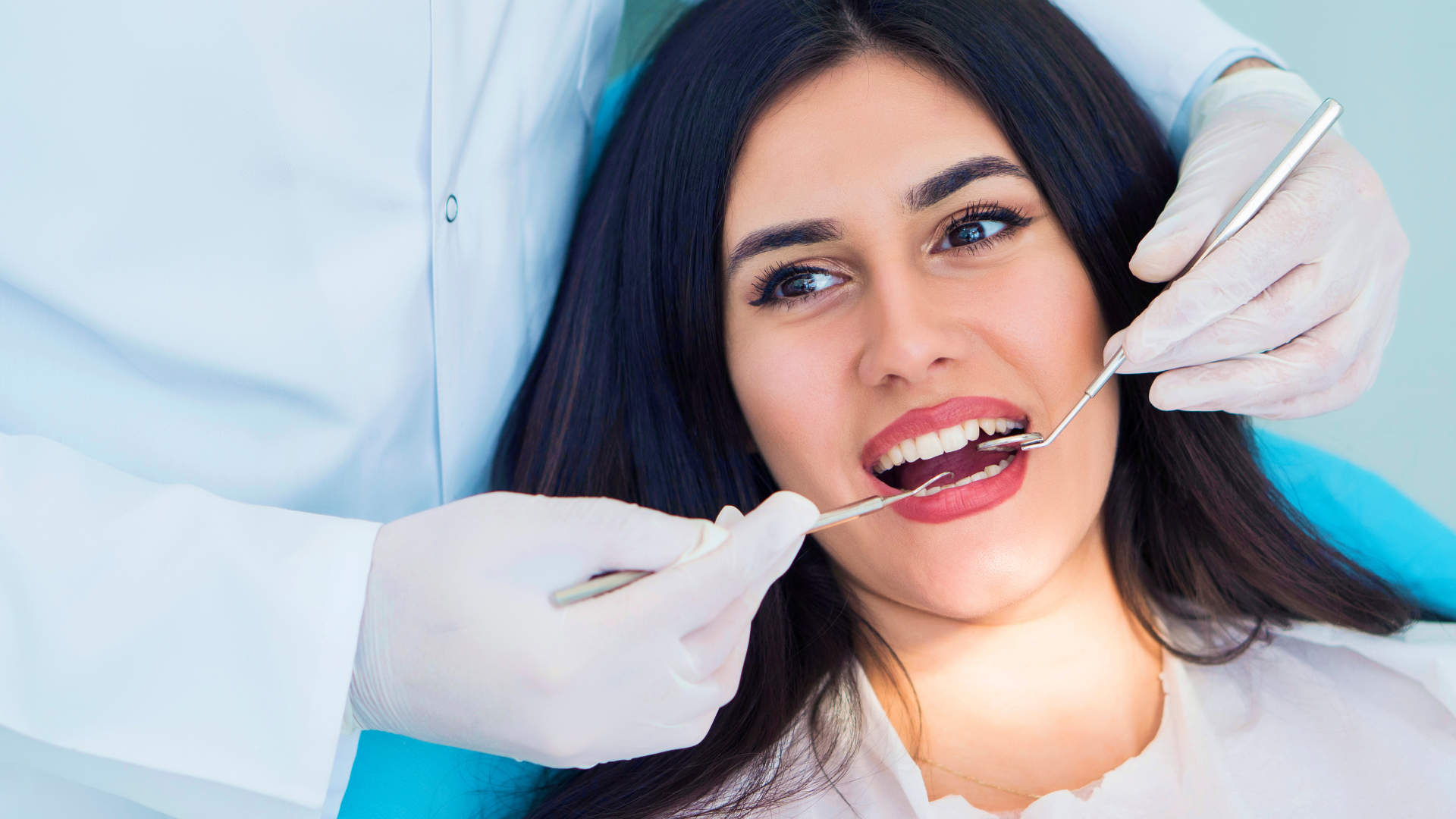 A woman is sitting in a dental chair looking at her teeth in a mirror.