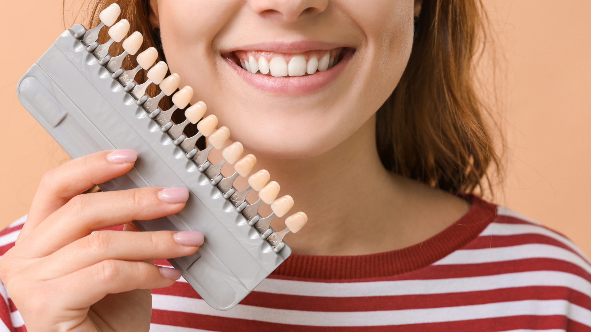 A woman is holding a tooth color chart in front of her mouth.