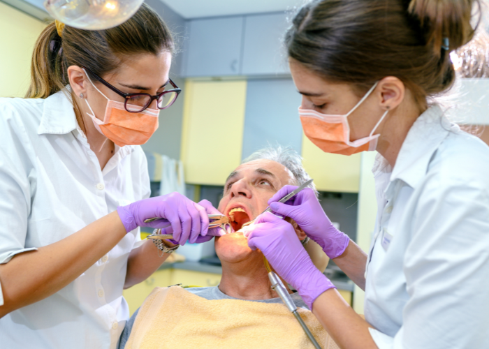 Two female dentists are examining a man 's teeth in a dental office.