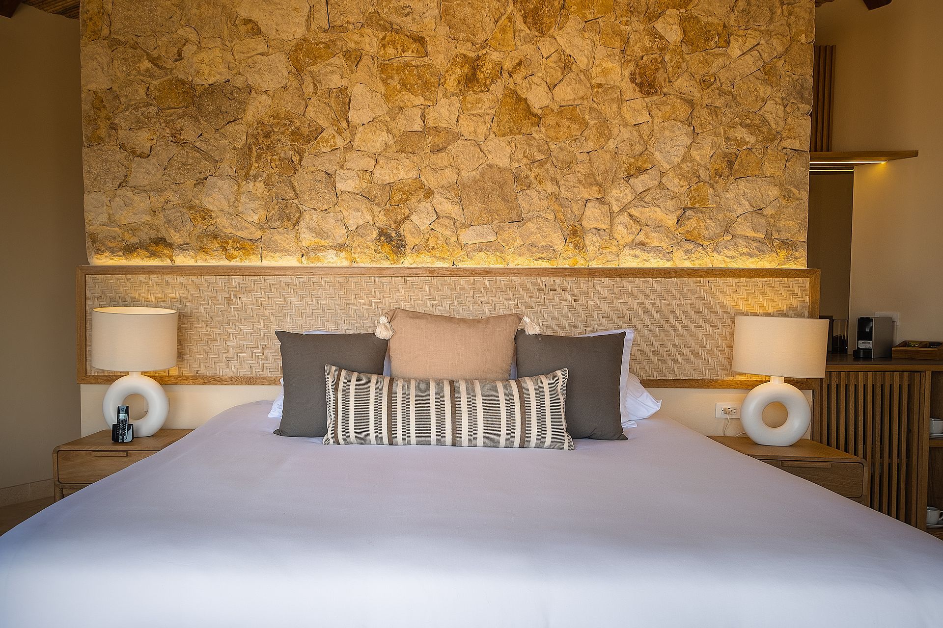 Accommodation in San Antero, Colombia, with a spacious bed, stone wall, bedside lamps, and nightstand.