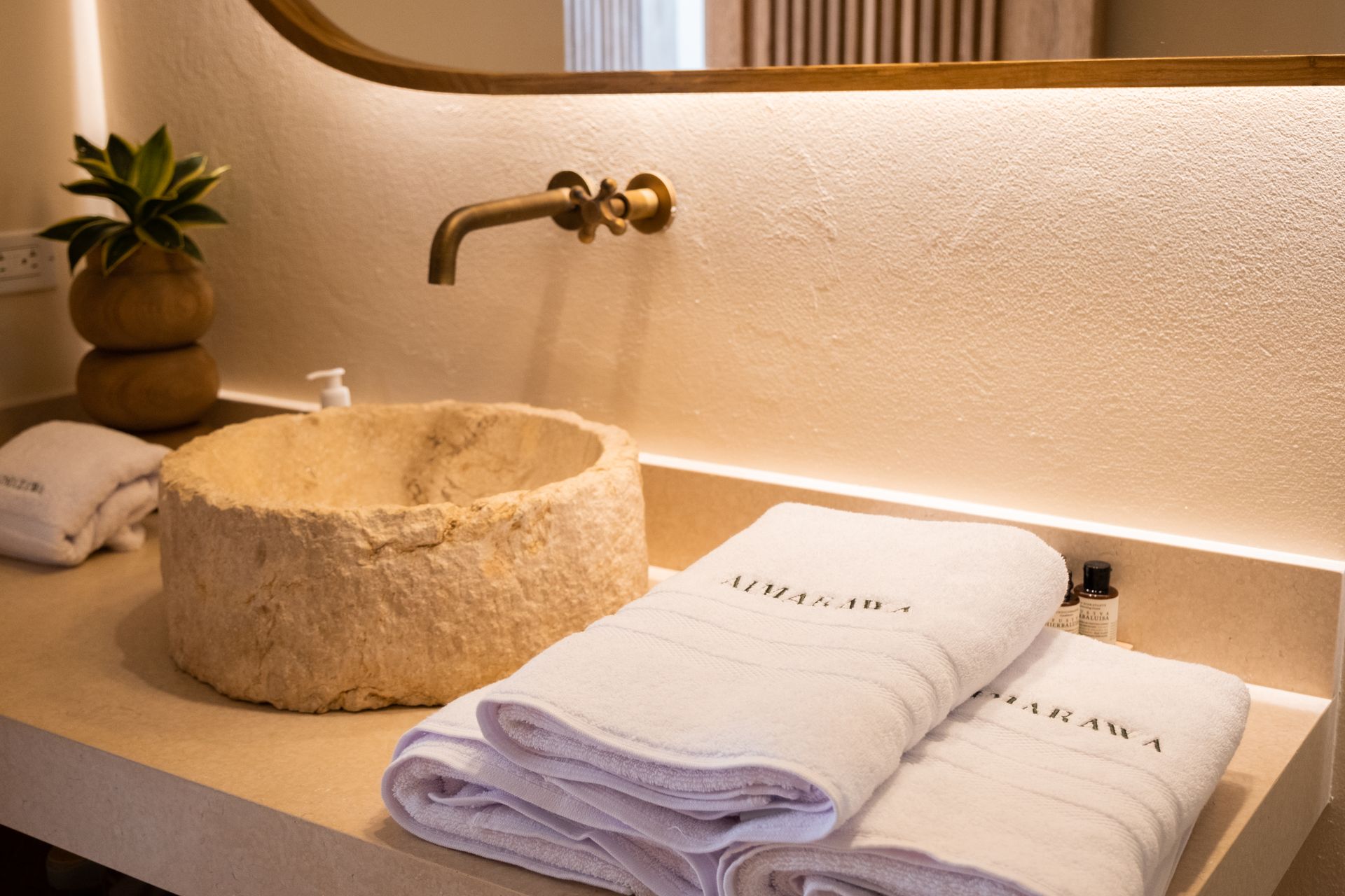 Hotel bathroom in San Antero, Córdoba with a stone sink, light towels, gold faucet, and warm lighting.