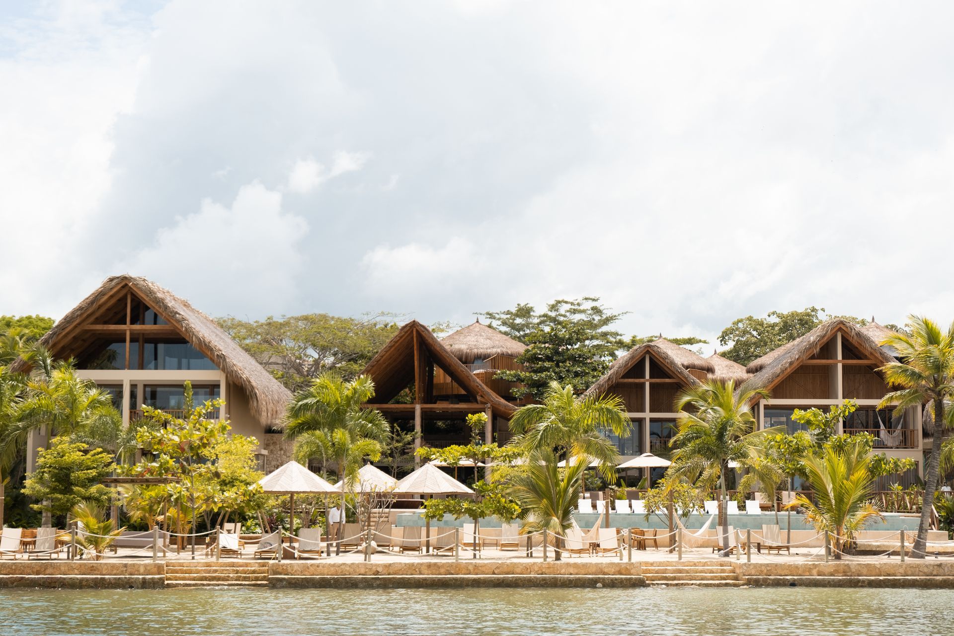 hotel frente al mar en punta bolívar san antero con cabañas de palma, piscina, sombrillas y palmeras.