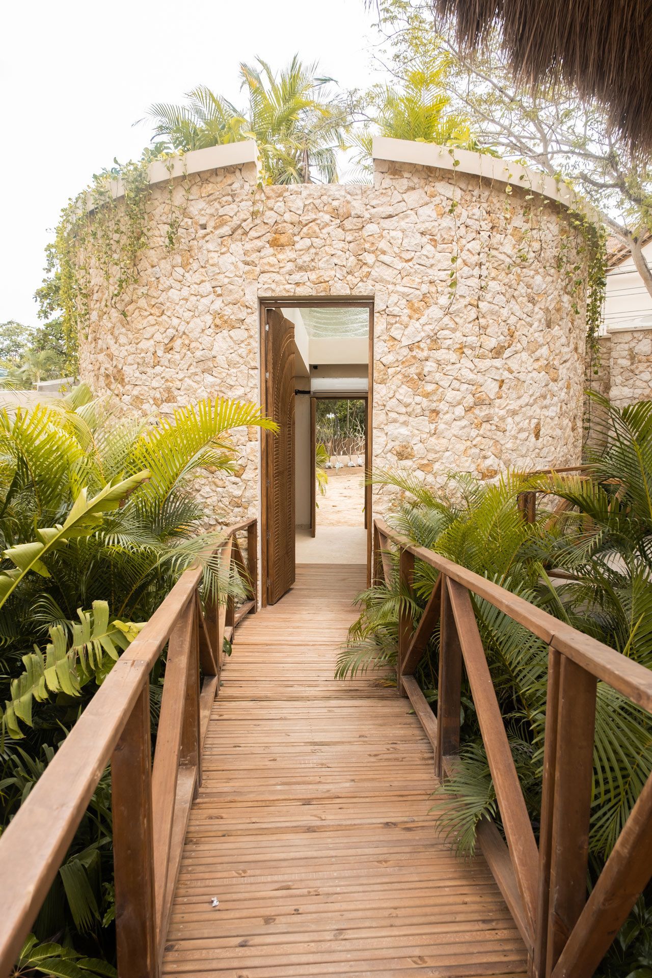 Entrance to Aimarawa in San Antero with wooden walkway, tropical plants, and stone façade.
