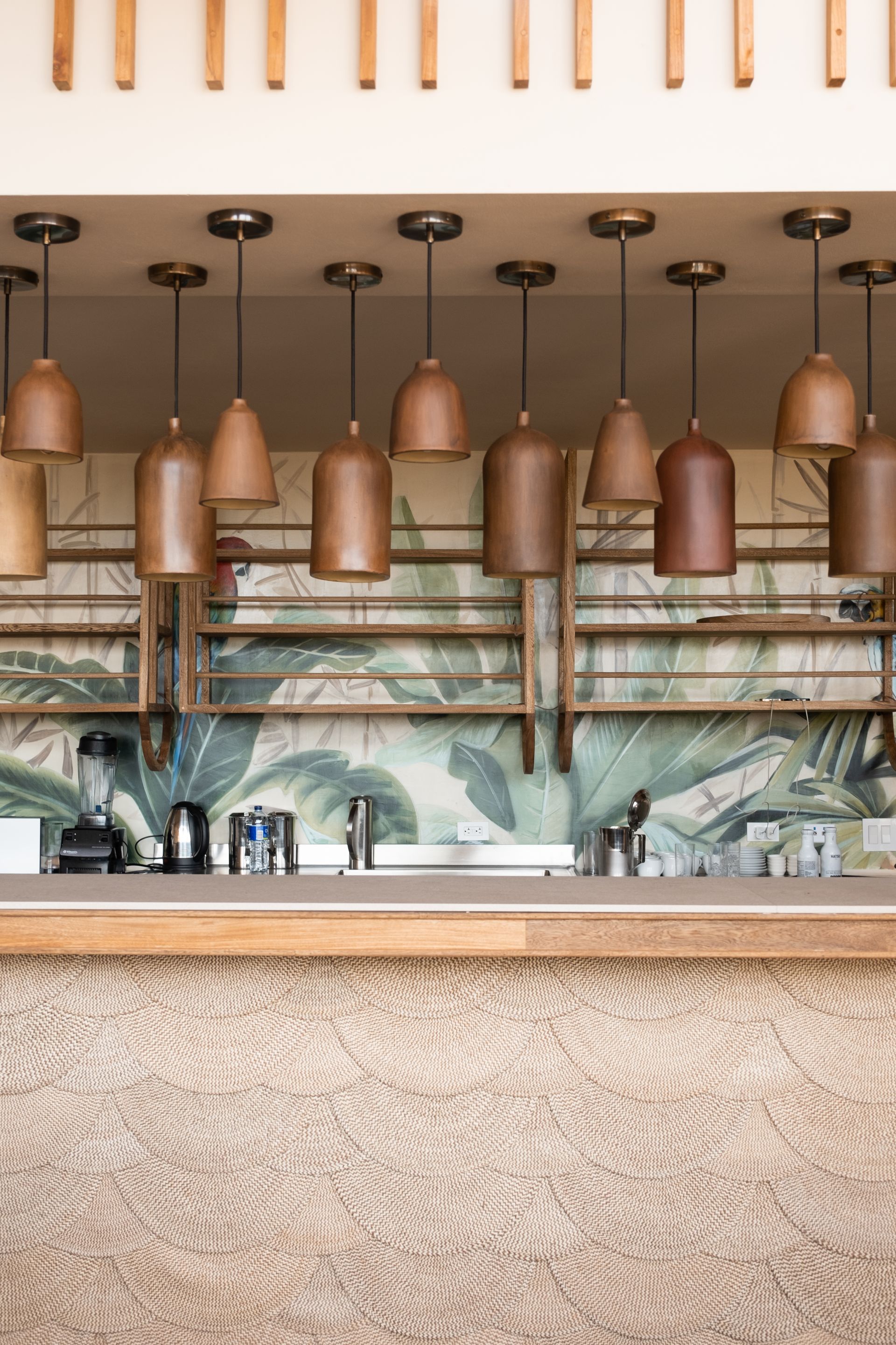 Bar on the beach Aimarawa with hanging clay lamps, wooden shelves, tropical wall art, and woven counter.