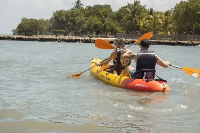 Turistas practicando kayak frente al Hotel Aimarawa, rodeados de aguas tranquilas y palmeras tropicales