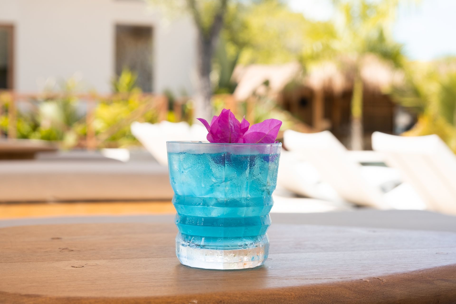 Blue cocktail with magenta flowers served poolside at Aimarawa.