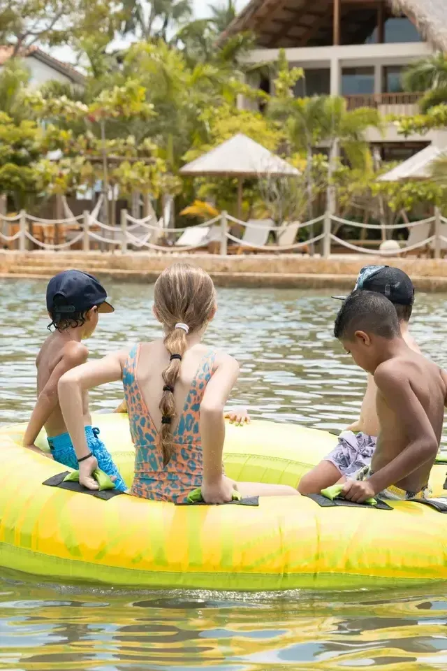 Niños en flotador amarillo frente a Aimarawa, con vegetación y zonas de descanso de hoteles en san antero.