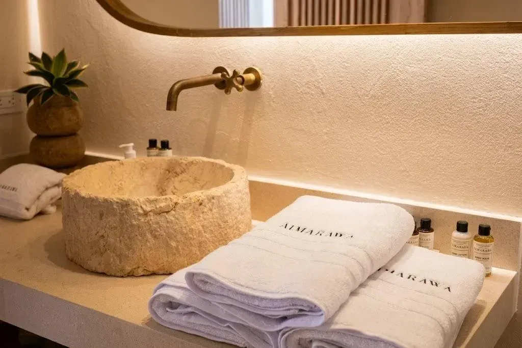 Baño de Hotel en San Antero Córdoba con lavamanos de piedra, toallas claras, grifería dorada y luz cálida.