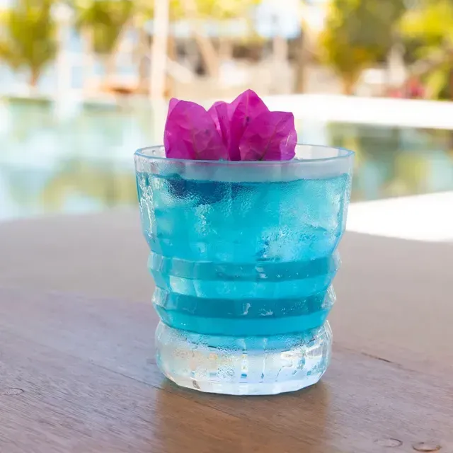Cóctel azul con flores magenta servido junto a la piscina en Hotel Aimarawa San Antero.