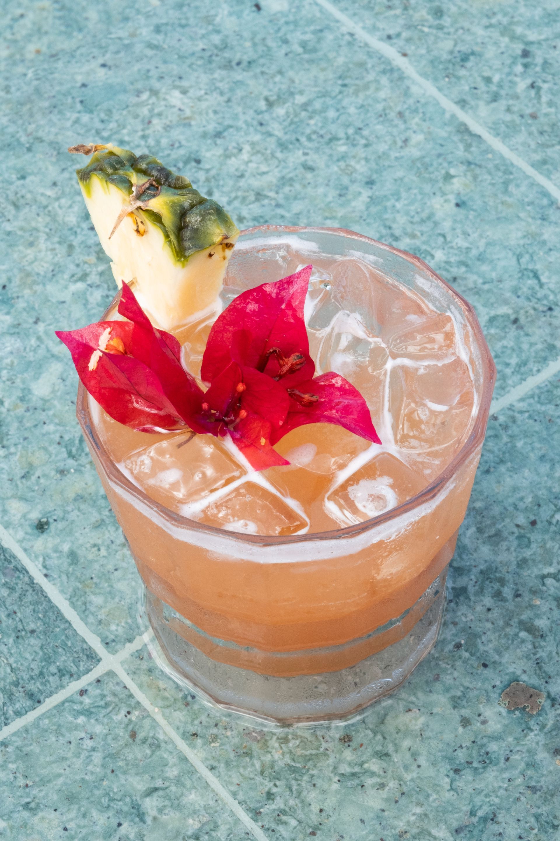 Cocktail with pineapple, red flower, and ice on a blue surface at Aimarawa’s bar.