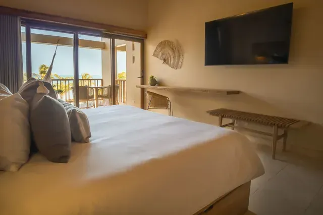 Hotel en San Antero Córdoba con cama amplia, escritorio de madera, ventanal y balcón frente al mar.