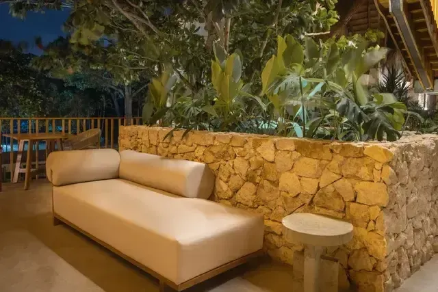 Terraza lounge del Hotel Aimarawa en San Antero con sofá beige, muro de piedra y vegetación tropical.