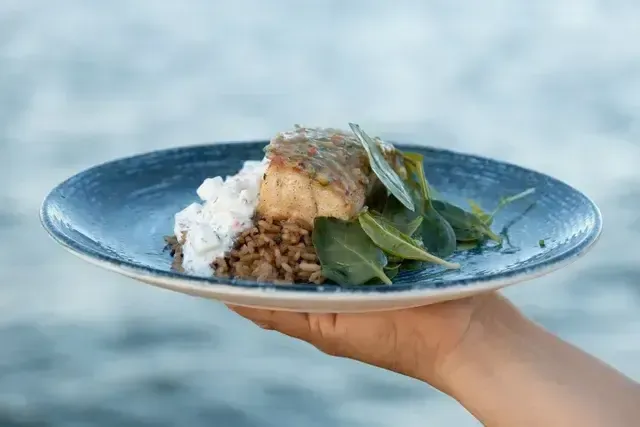 Plato de pescado con arroz con coco y hojas verdes servido frente al mar en Guadua, restaurante de Aimarawa.
