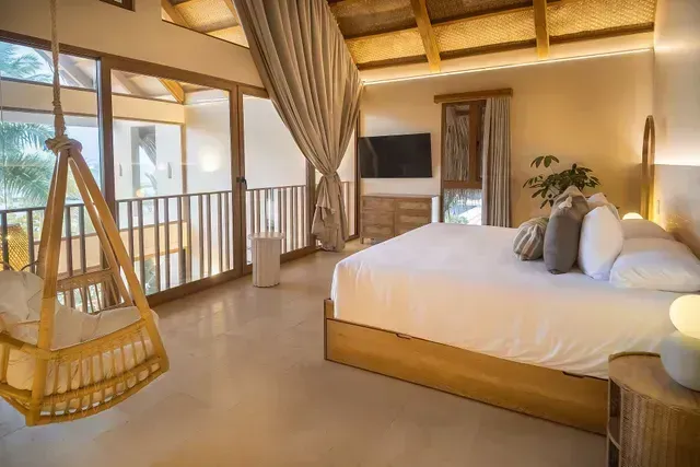 habitación de hotel en san antero con cama amplia, silla colgante, techo de madera y ventanales hacia el exterior.