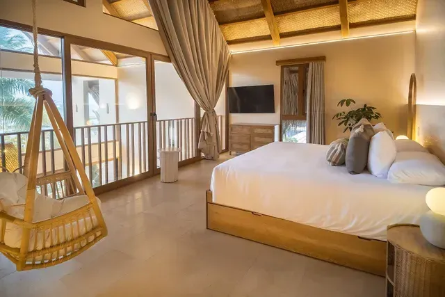 Quarto do Hotel Aimarawa na Colômbia com cama king, rede suspensa e varanda de madeira.