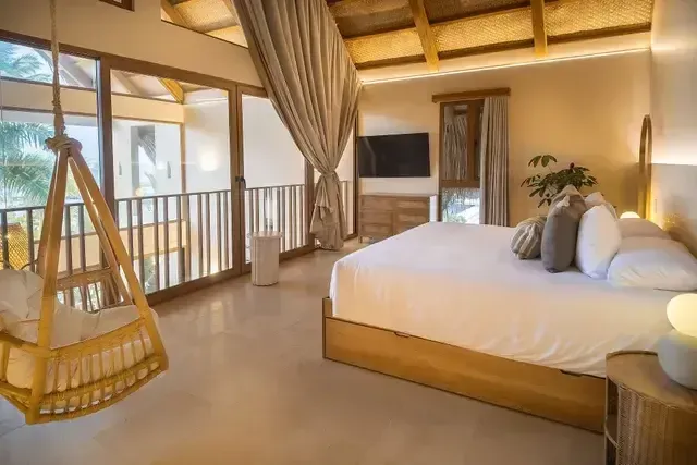 Habitación de Aimarawa, hotel en san antero, con cama king, silla colgante, ventanales y techo de palma