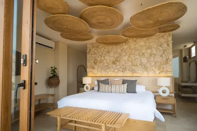 Quarto de hotel em San Antero Córdoba com cama ampla, teto decorado, parede de pedra e atmosfera serena.