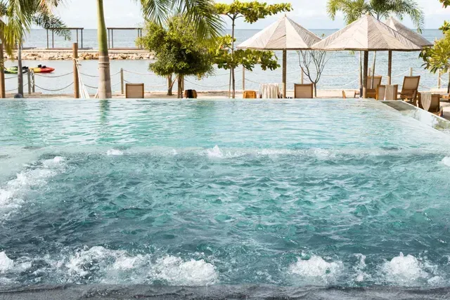 Piscina con burbujas de hotel frente al mar, sombrillas, asoleadoras y palmeras en Aimarawa