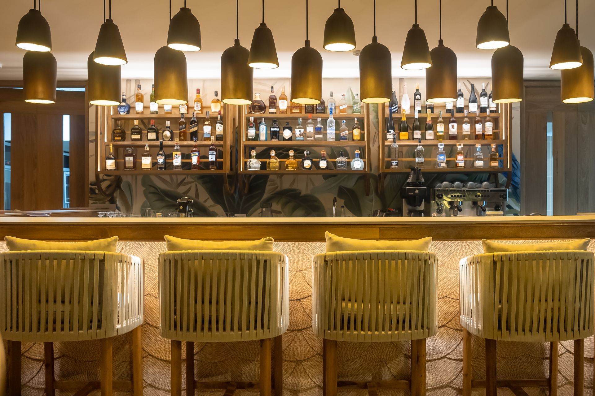 Bar Ara Macao no Hotel Aimarawa, com bancos altos, bebidas, luminárias pendentes e balcão iluminado.