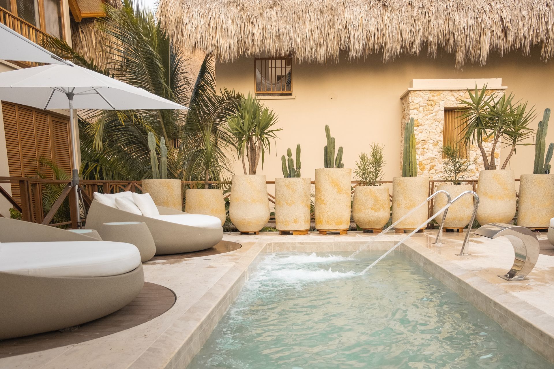 Aimarawa, a hotel with pool in San Antero, featuring white loungers, umbrellas, palm trees, cacti, and thatched roofs.