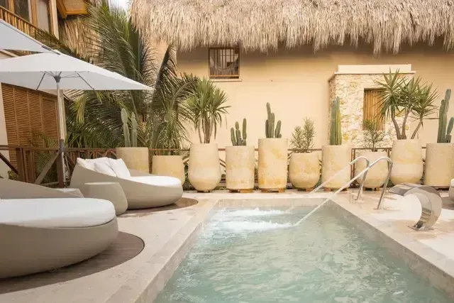 Aimarawa, hotel with pool in San Antero, featuring white loungers, umbrellas, palm trees, and thatched roofs.