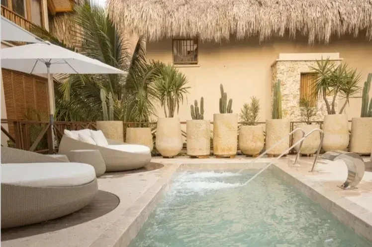 Aimarawa, hotel con piscina en san antero, con camastros blancos, sombrilla, palmeras, cactus y techo de palma.