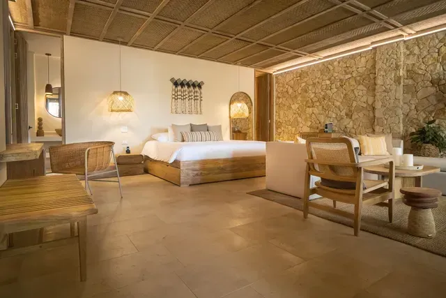 hoteles en san antero cordoba con suite de cama grande, sofá, mesa de madera, techo tejido y muro de piedra.