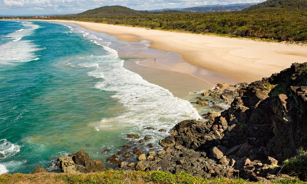 Scenic view of a sandy beach with turquoise water, breaking waves, and a forest backdrop. — North Coast Stock Feeds in Wardell, NSW