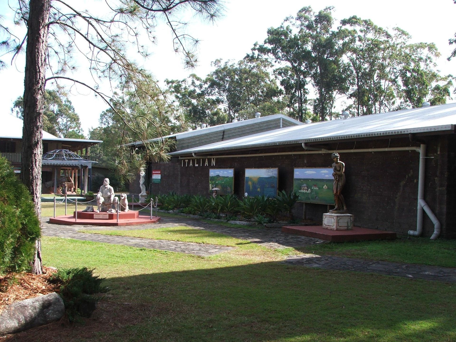 Museum buildings with statues and display panels, set in a grassy courtyard. — North Coast Stock Feeds in Wardell, NSW