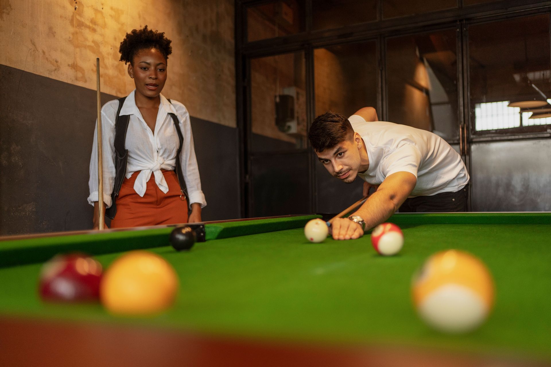 Two people playing pool, with one lining up a shot across the table.