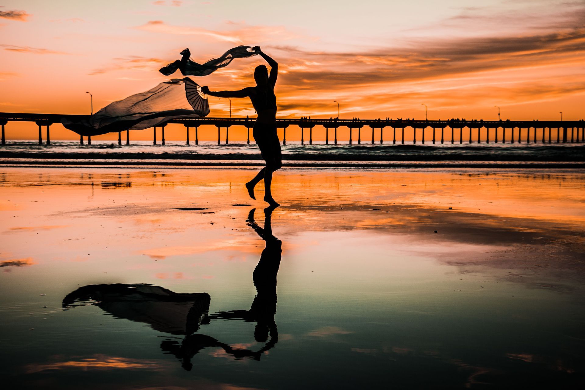 Person moving with flowing fabric on a beach at sunset.