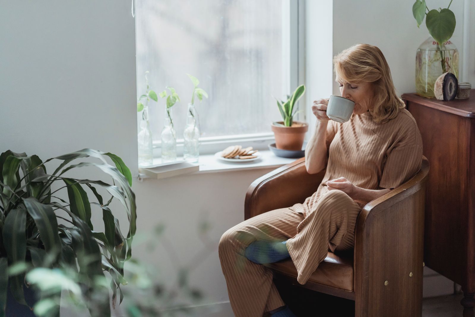 Woman sitting quietly near a window with a warm drink.
