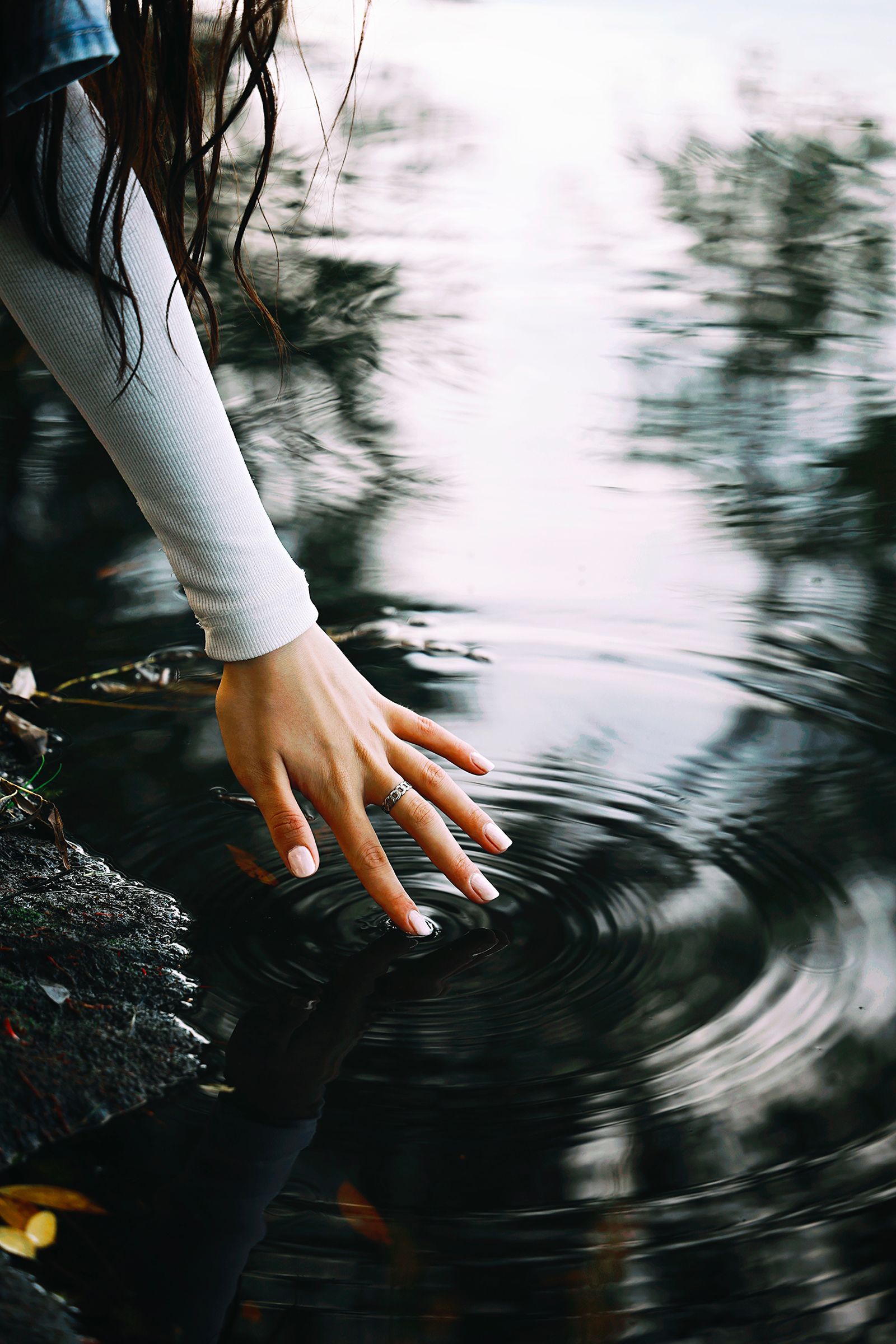 Hand touching water as ripples spread across the surface.