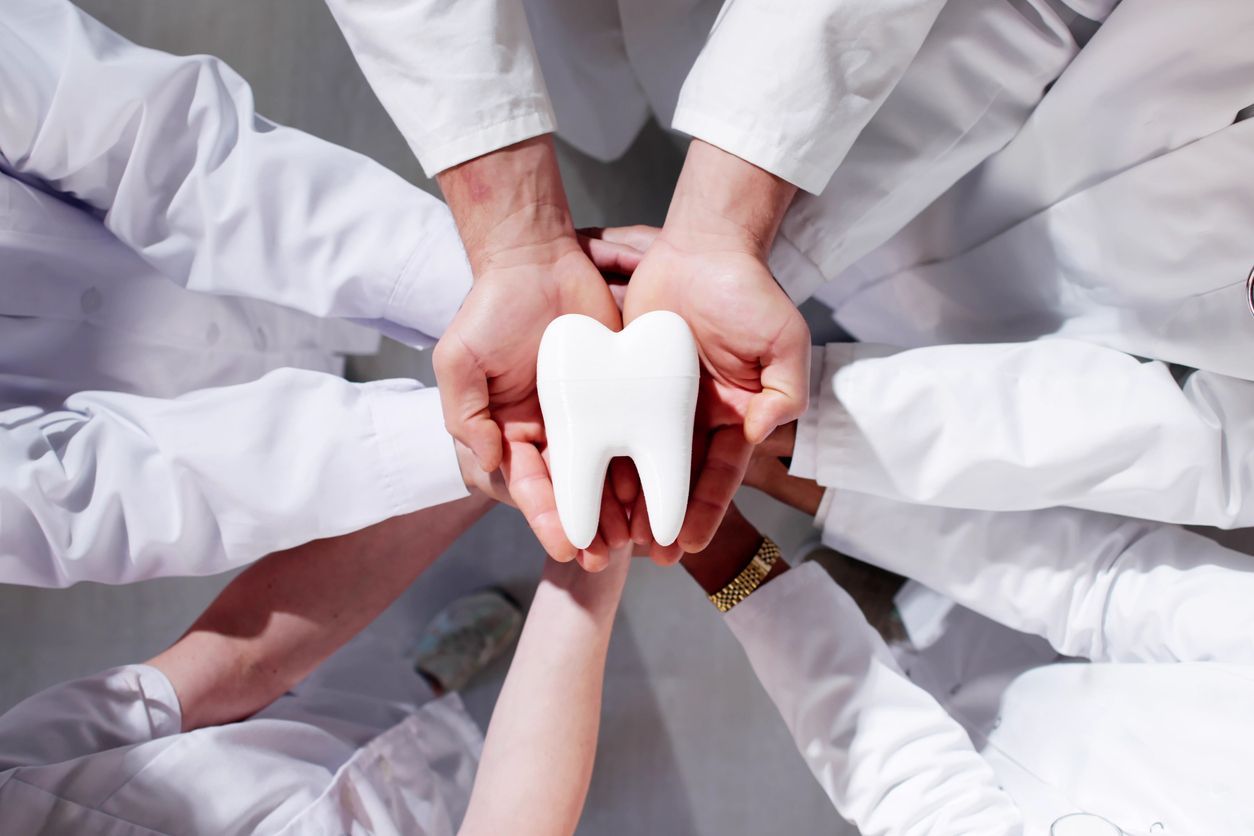 Hands of people in white coats hold a large white tooth.
