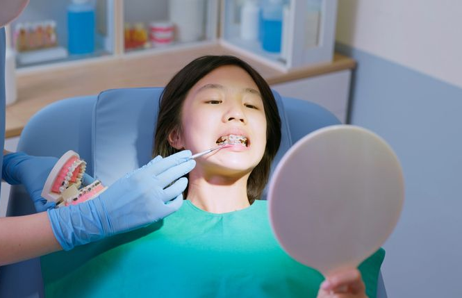 Girl with braces at a dental visit, looking in a mirror. Dentist examining teeth with an instrument.