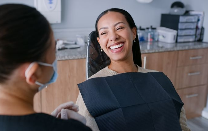 Woman smiling widely at dentist in a dental office. Dentist wearing mask, gloves.