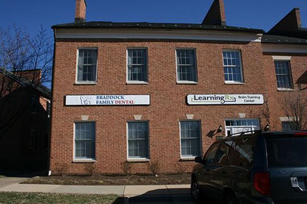Two-story brick building with signs for a dental office and a tutoring center. A car is parked in front.