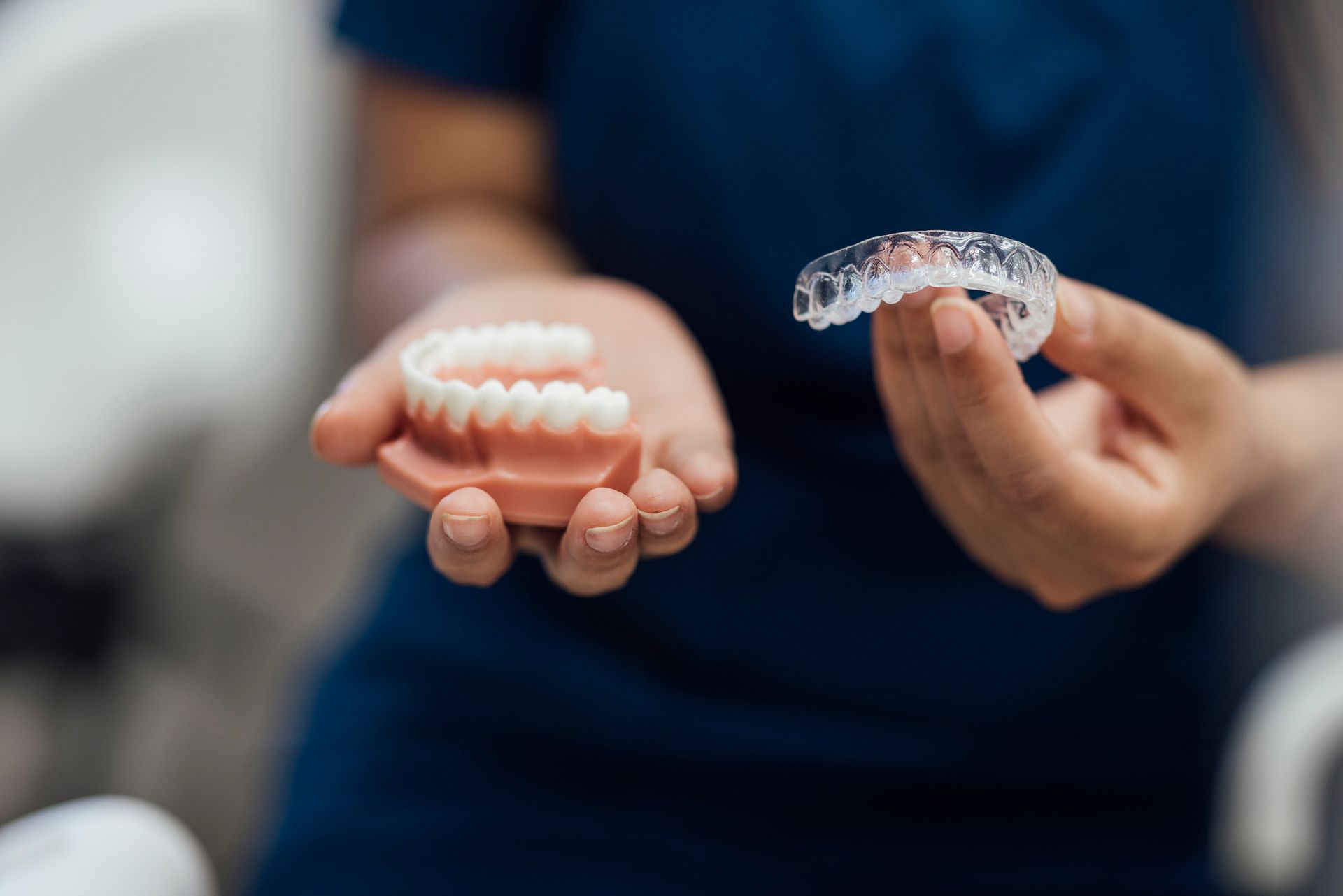 Person holding a dental model and a clear mouthguard, possibly in a dentist's office.