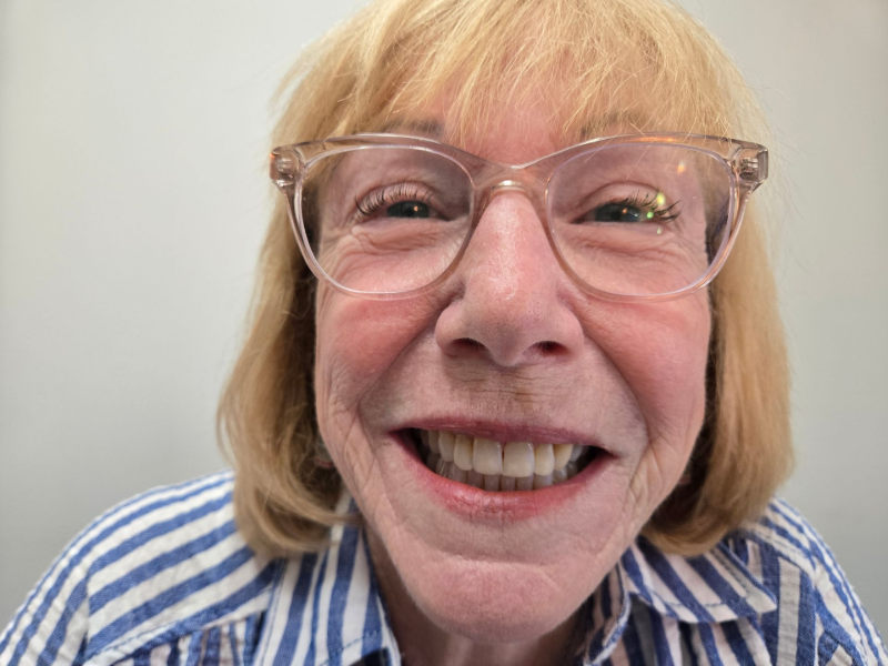 Smiling person with glasses and blond hair in a blue-and-white striped shirt