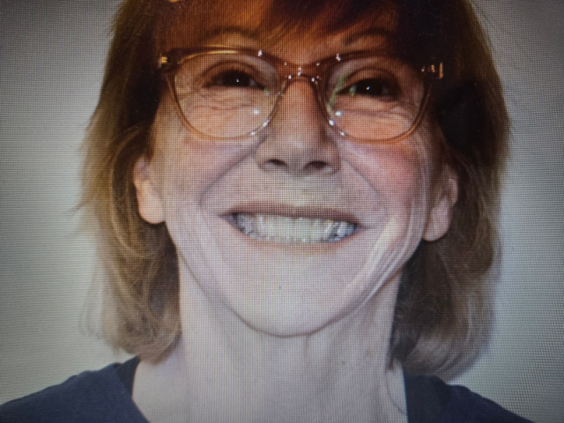 Smiling person wearing glasses and a dark shirt against a plain background