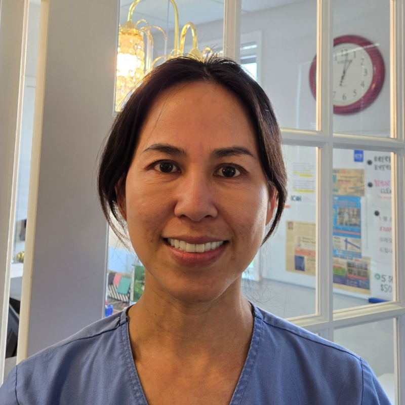 Thuy smiling in blue scrubs standing in a bright indoor hallway