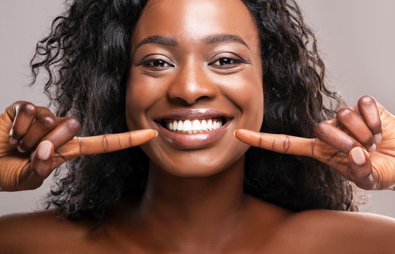 A woman is smiling and pointing at her teeth.