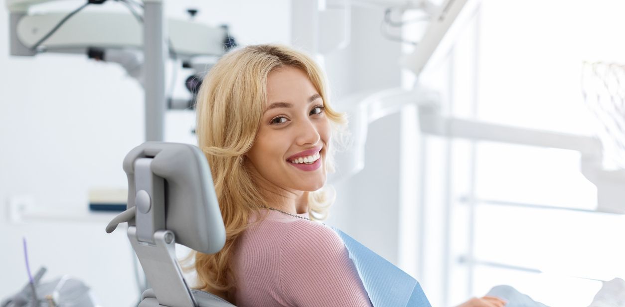 A woman is smiling while sitting in a dental chair.