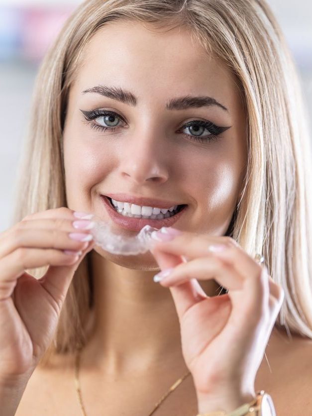 A woman is smiling while holding a clear brace in her mouth.