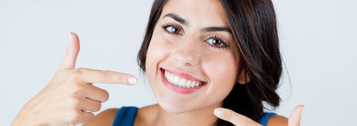 A woman is pointing at her teeth and smiling.