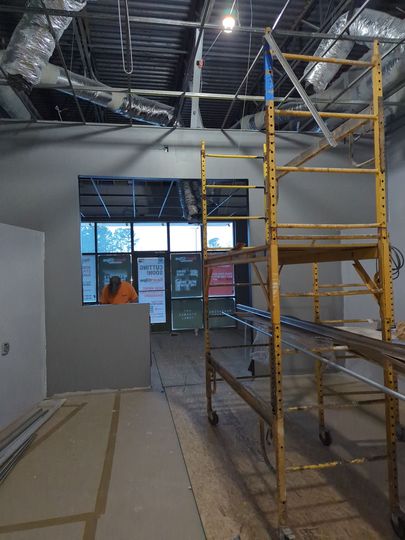 A construction site interior featuring a yellow scaffolding tower and a person in an orange shirt standing near a window.
